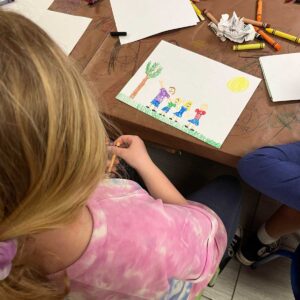 over the shoulder view of a child coloring a family poster.